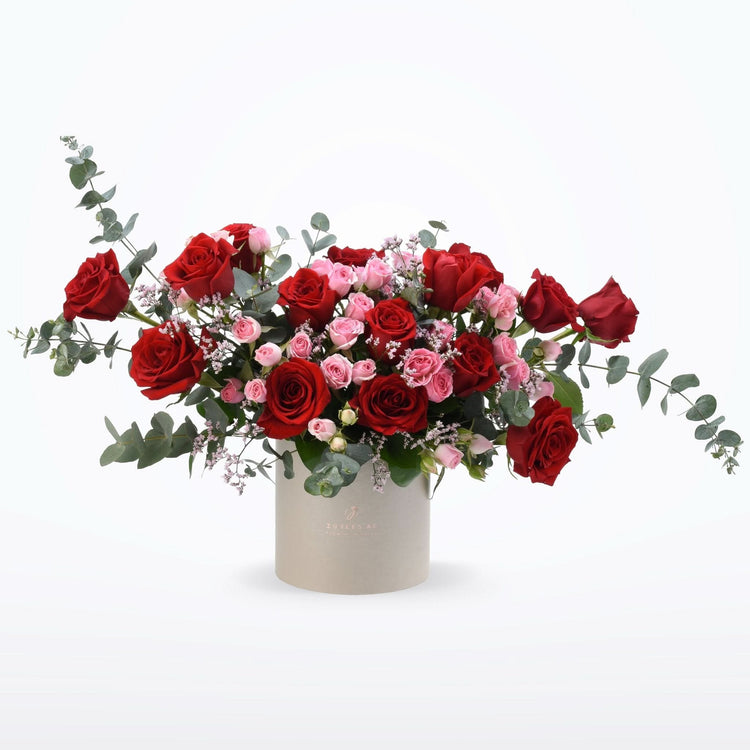 Luxurious red and pink roses with eucalyptus in minimalist beige cylinder.