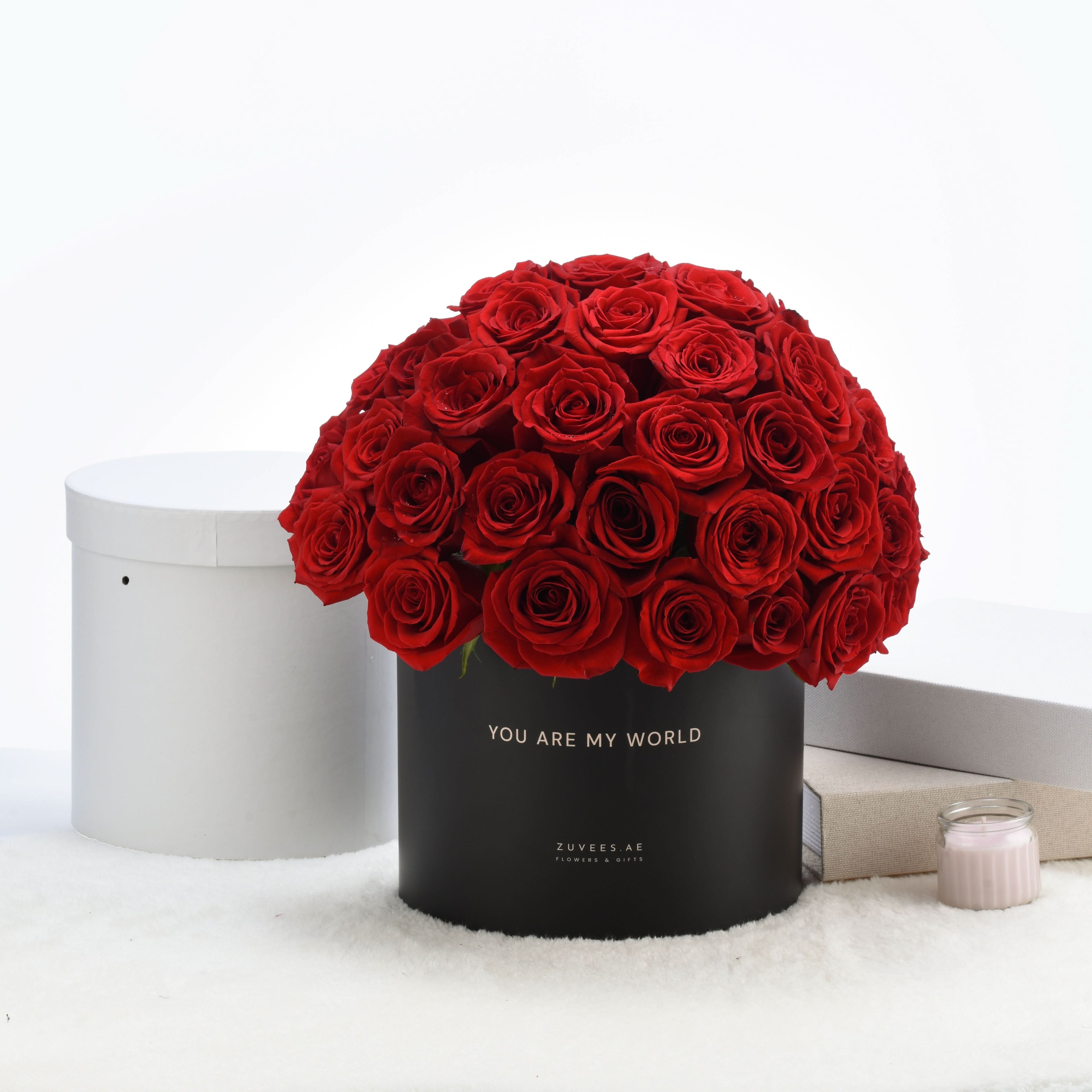 Vibrant red roses in black box reading "You Are My World," elegant white backdrop.