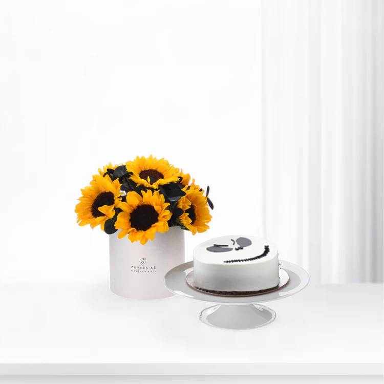 Vibrant sunflowers in white vase beside minimalist white cake with black smiley face.