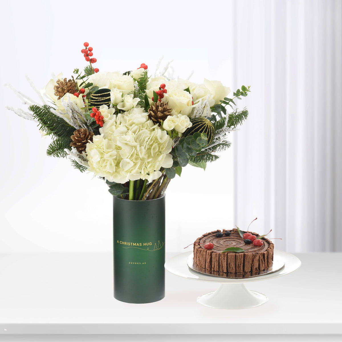 Elegant white roses, hydrangeas, pinecones in green vase beside chocolate Yule log cake.