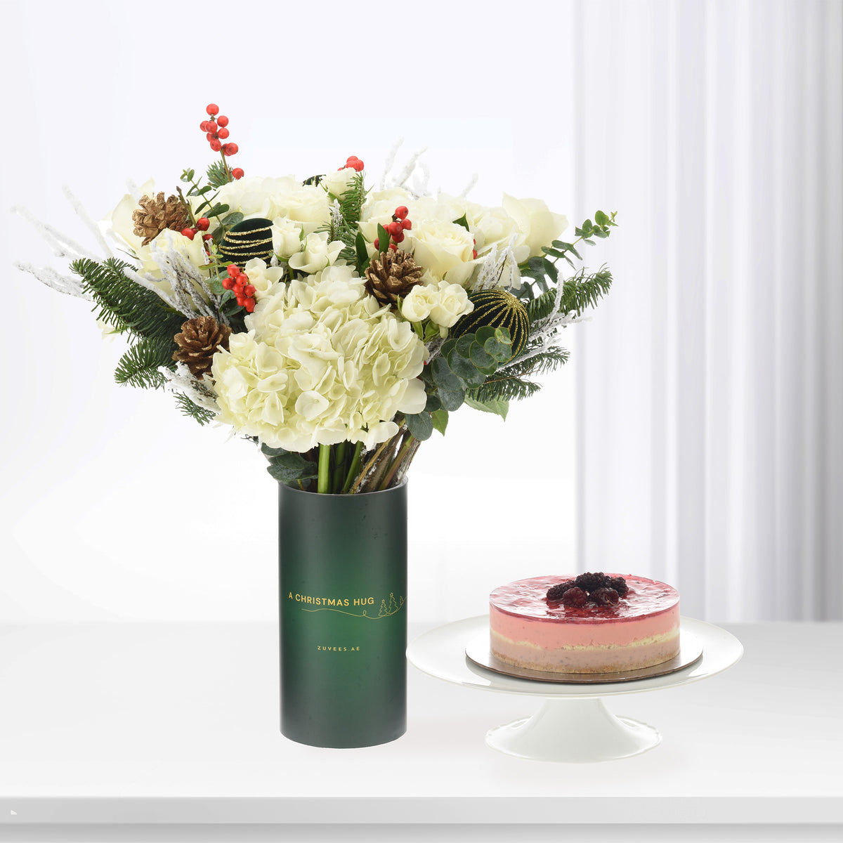 White roses and hydrangeas in green vase beside layered berry cake.