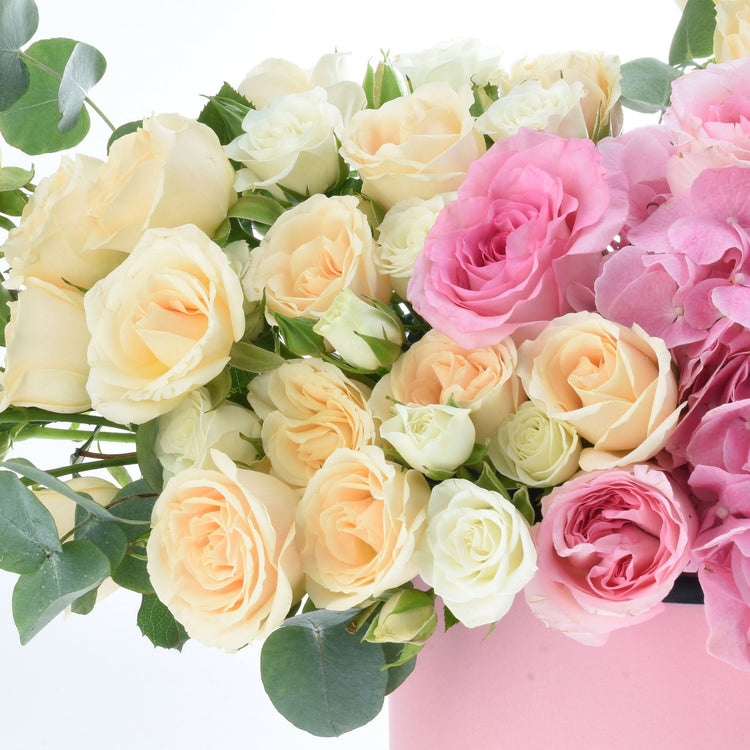 Cream, peach, and pink roses with eucalyptus in a soft pink vase.