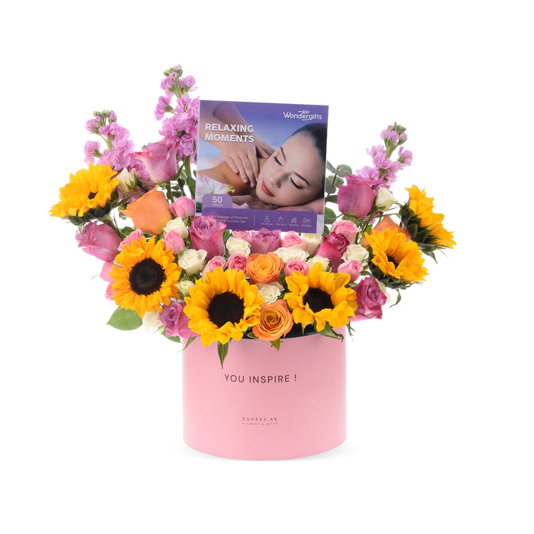 Vibrant sunflowers, roses, and pink blooms in a pink "YOU INSPIRE!" box with massage gift card.