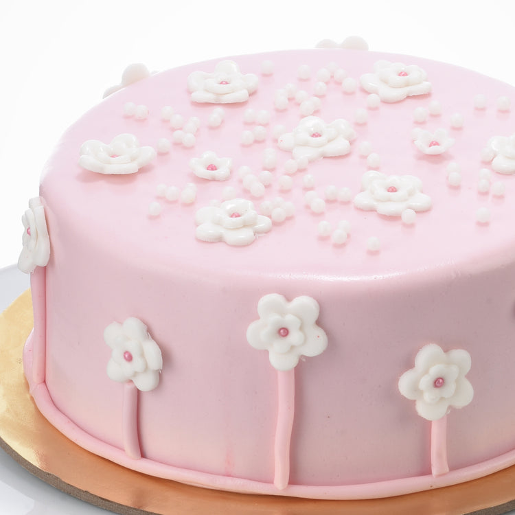 Soft pink cake adorned with white sugar flowers and pearl sprinkles.