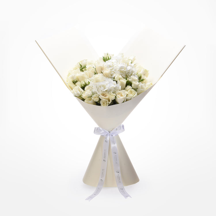 Elegant white rose bouquet with hydrangeas, wrapped in cream paper, tied with branded ribbon.