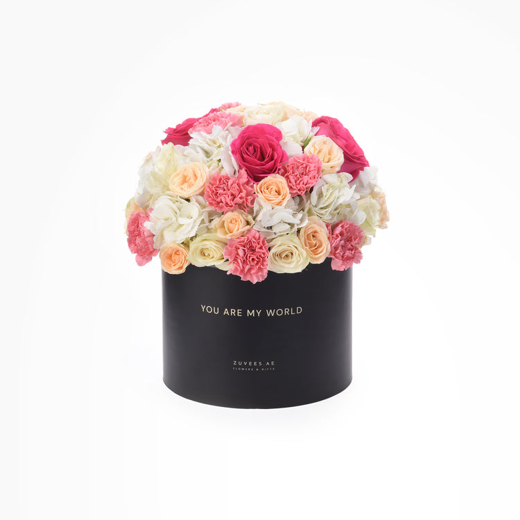 Black box holds vibrant pink, peach, and white roses and carnations.