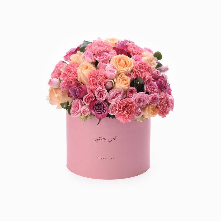 Pink cylindrical box overflowing with vibrant pink, peach, and purple roses and carnations.