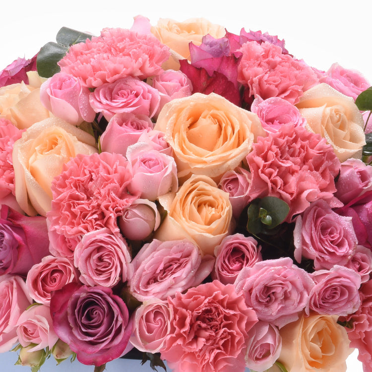 Pink, peach, and magenta roses with dewdrops, lush carnations, green leaves, soft pastel bouquet.