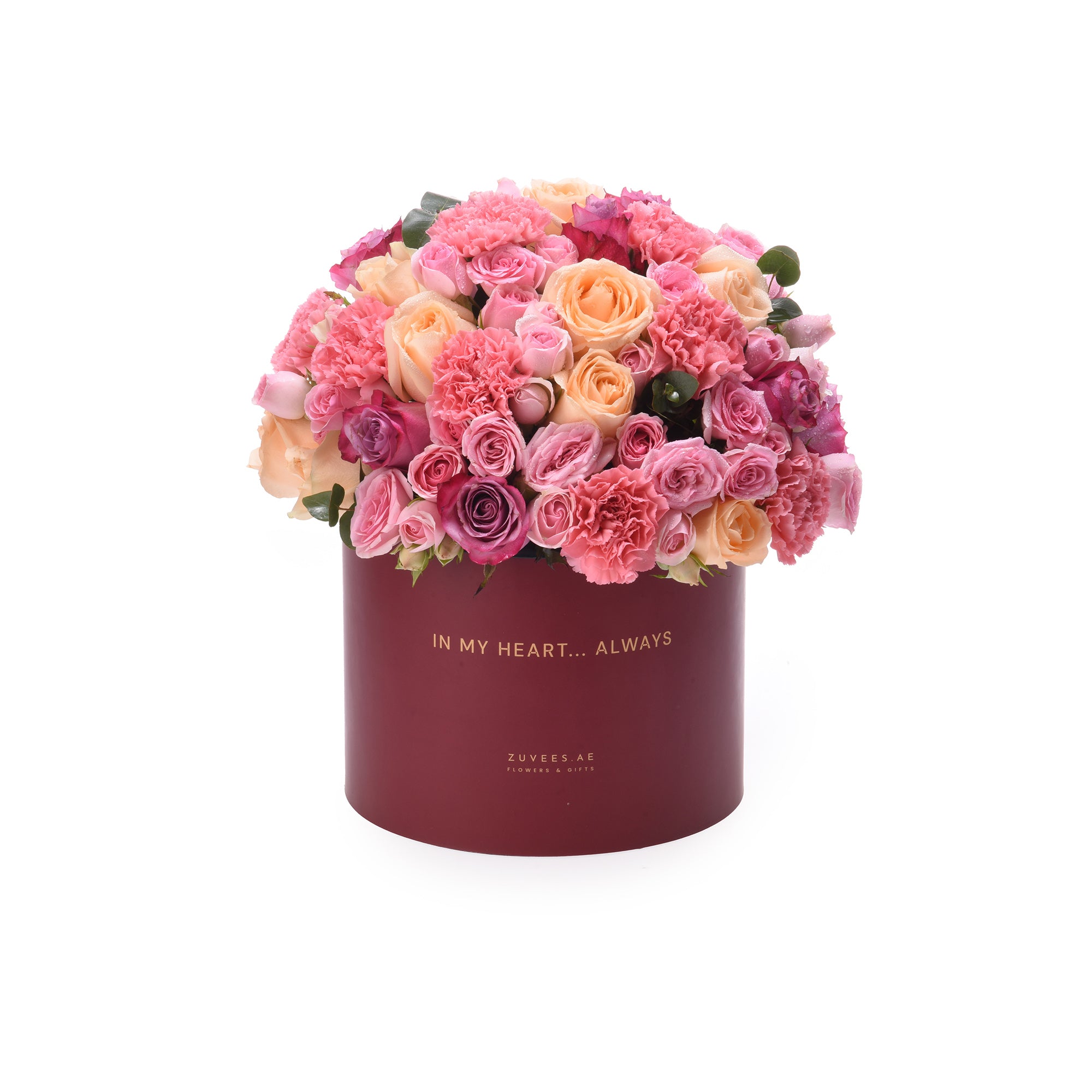 Vibrant pink, peach, and magenta roses and carnations overflowing from a deep burgundy hat box with gold "IN MY HEART... ALWAYS" text.