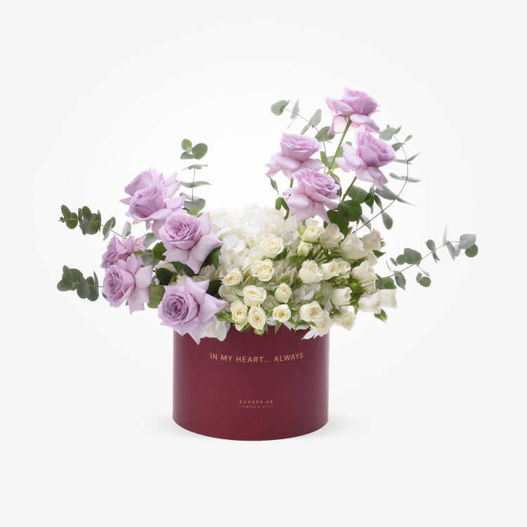 Elegant lavender roses and white blooms in burgundy box with gold text.