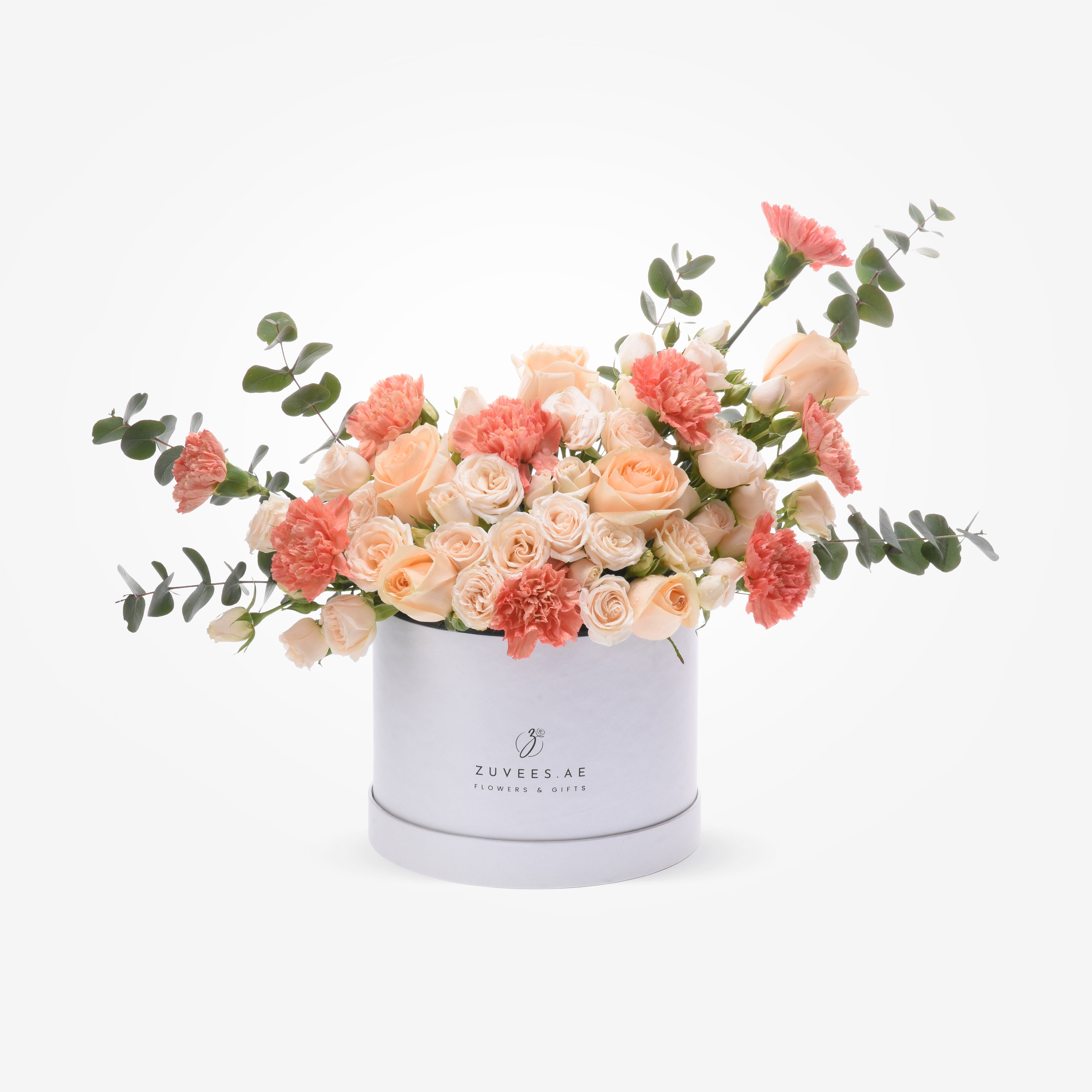 Soft peach roses and carnations in sleek white hat box with eucalyptus.