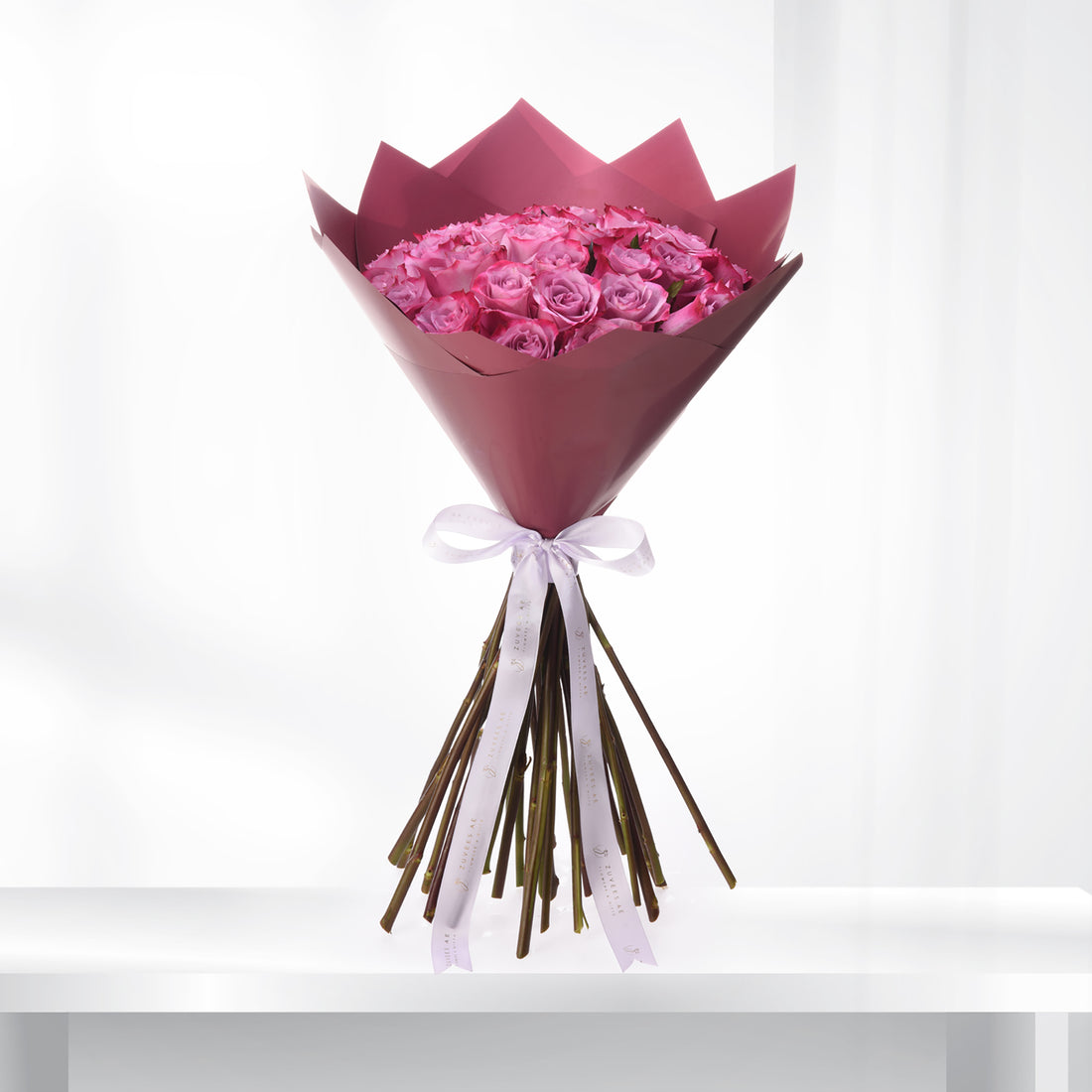 Vibrant pink roses in burgundy paper, elegantly tied with white ribbon.