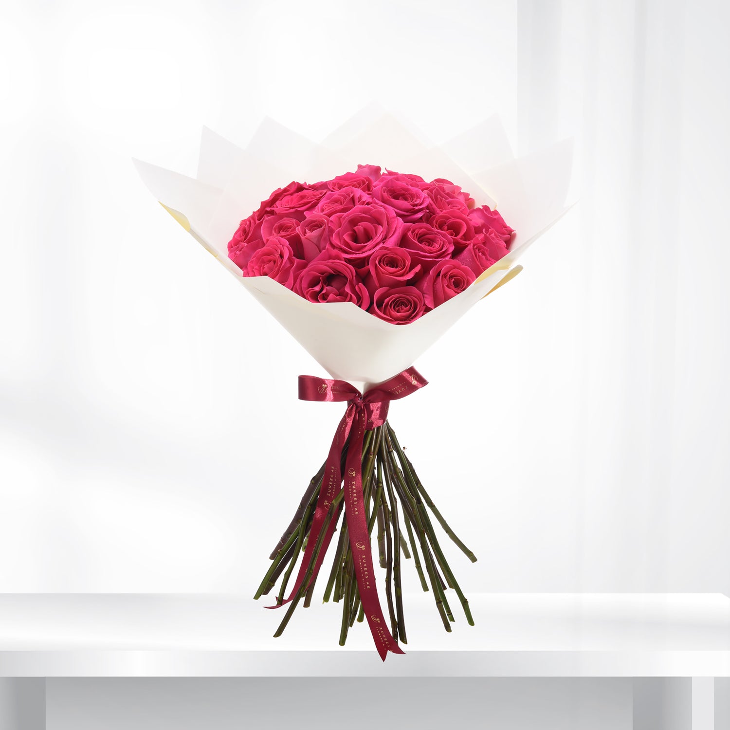 Vibrant fuchsia roses in crisp white paper, tied with burgundy ribbon.