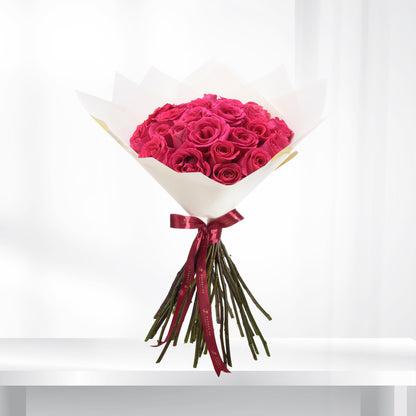 Vibrant fuchsia roses in crisp white paper, tied with burgundy ribbon.