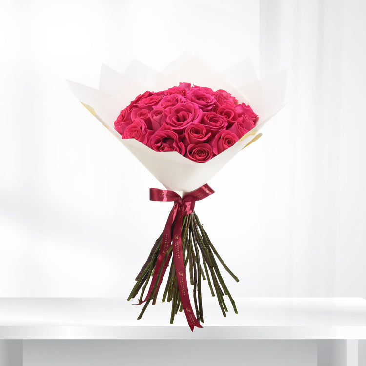 Vibrant fuchsia roses in crisp white paper, tied with burgundy ribbon.
