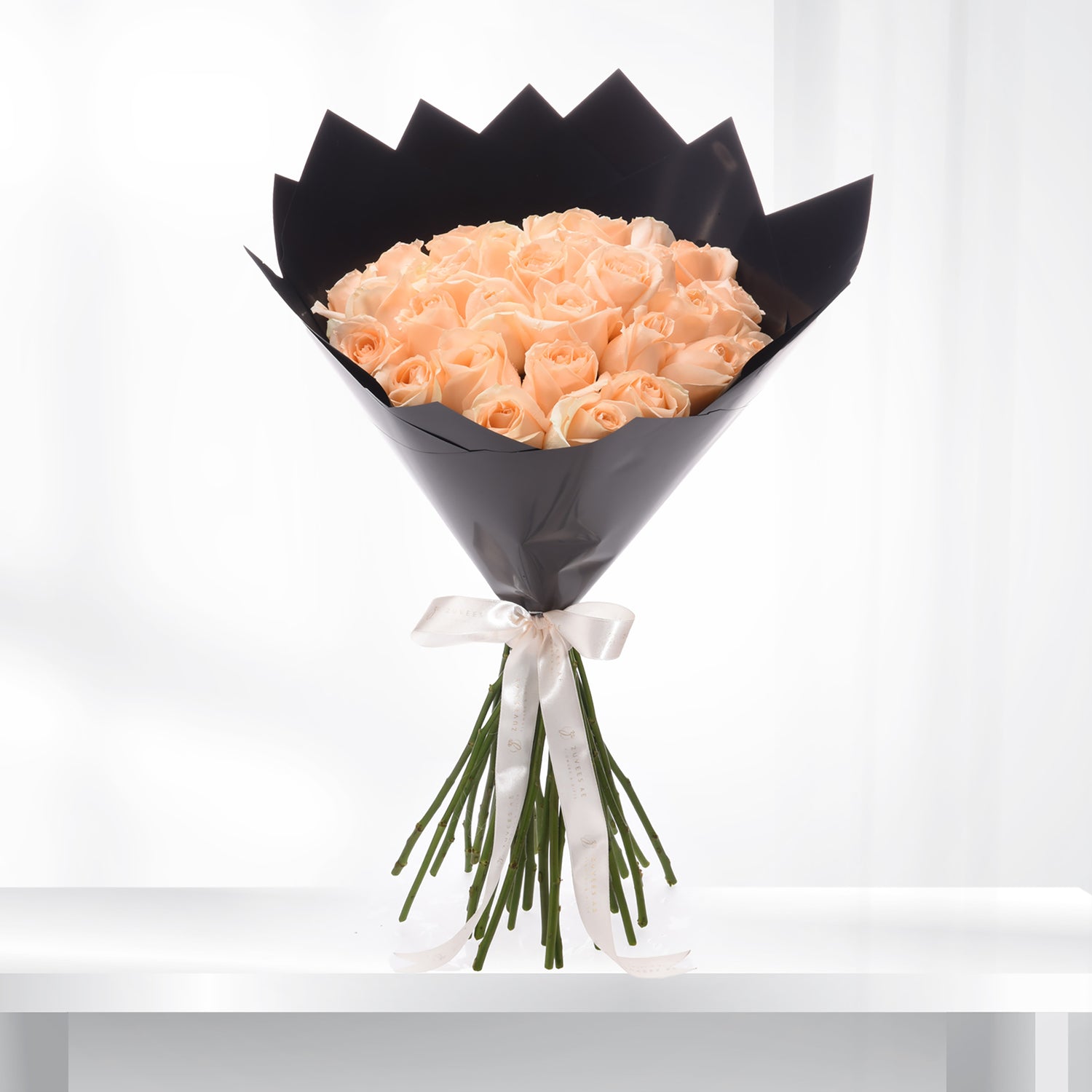 Soft peach roses in sleek black paper, tied with elegant white ribbon.