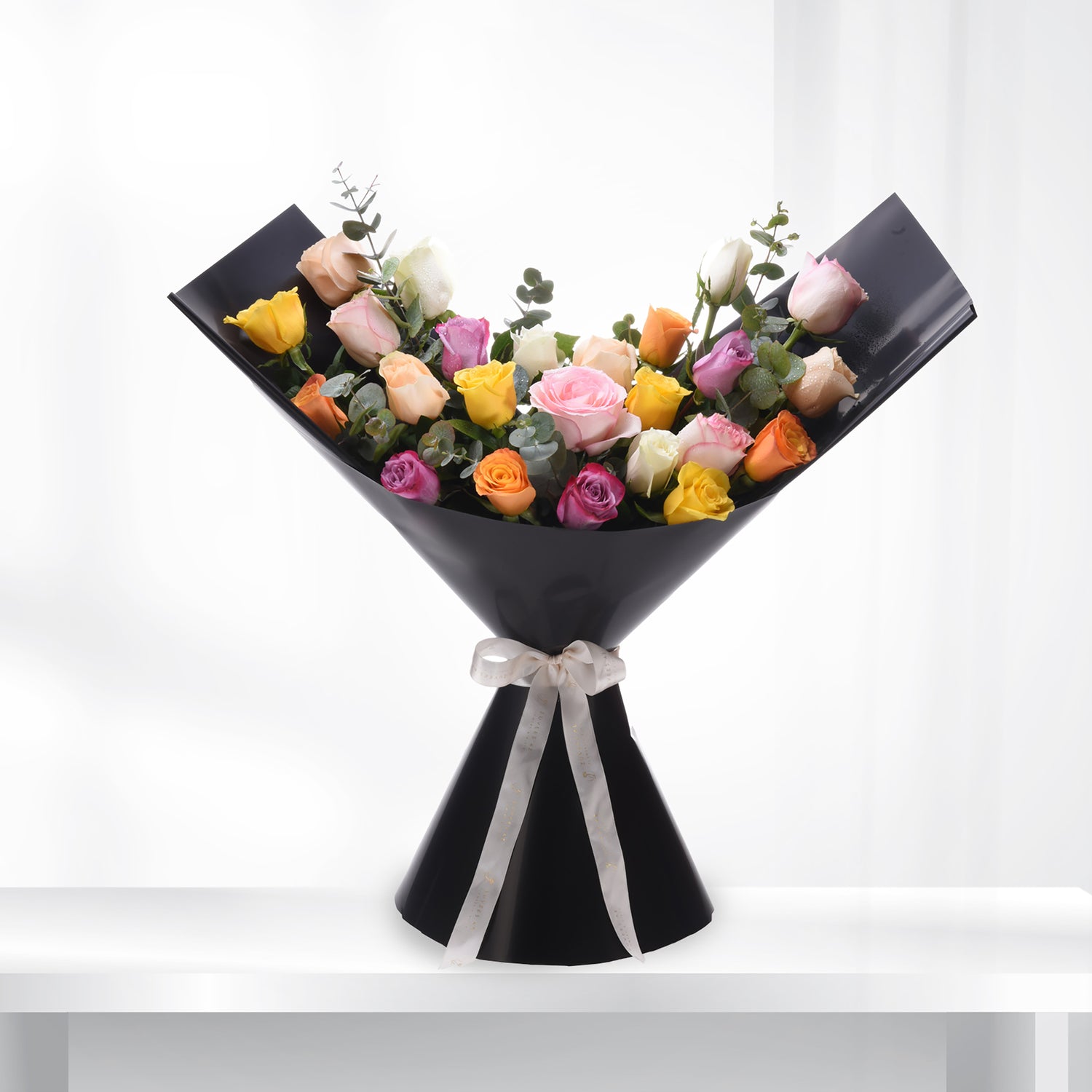 Vibrant multi-colored roses elegantly wrapped in sleek black paper with a delicate cream ribbon.