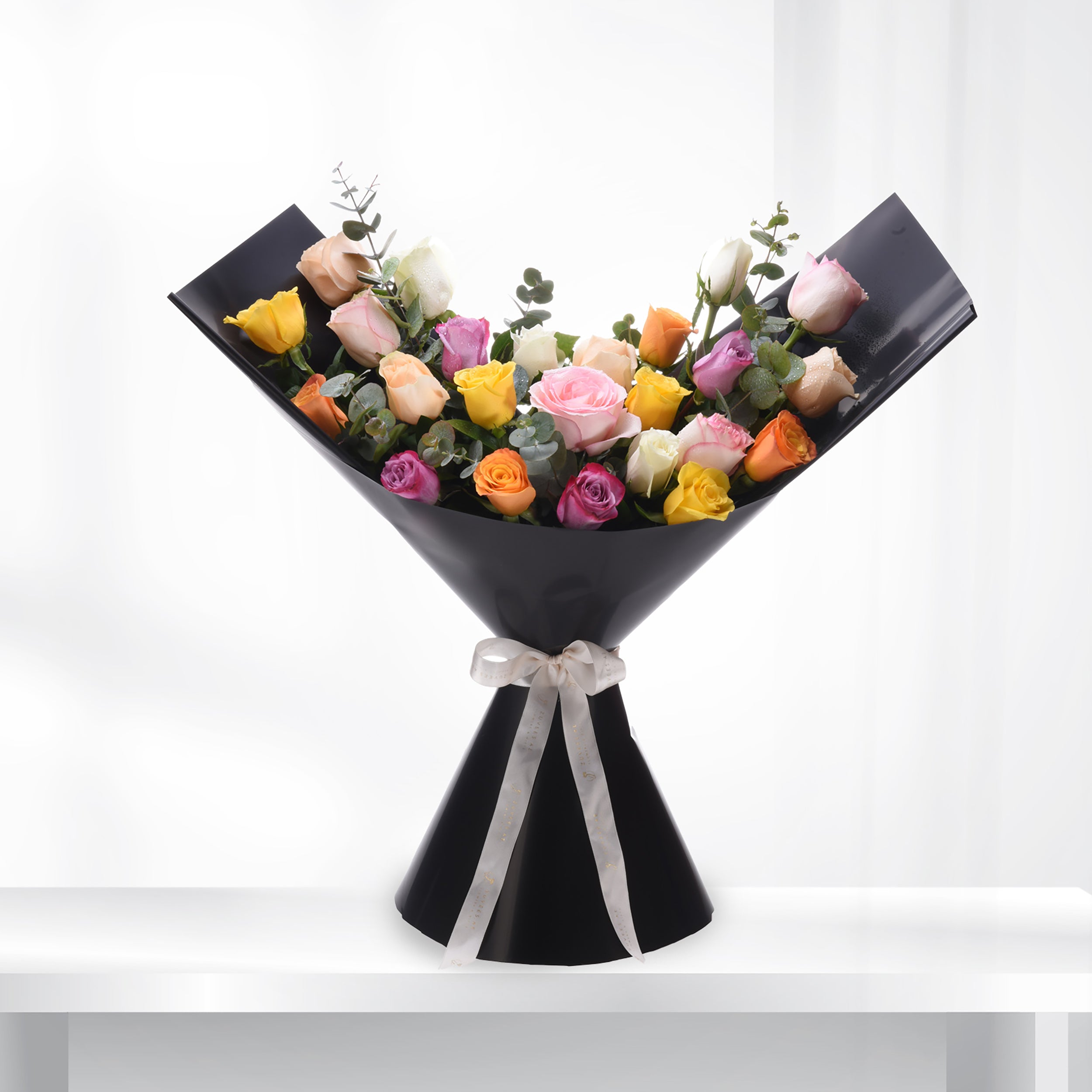 Vibrant multi-colored roses elegantly wrapped in sleek black paper with a delicate cream ribbon.