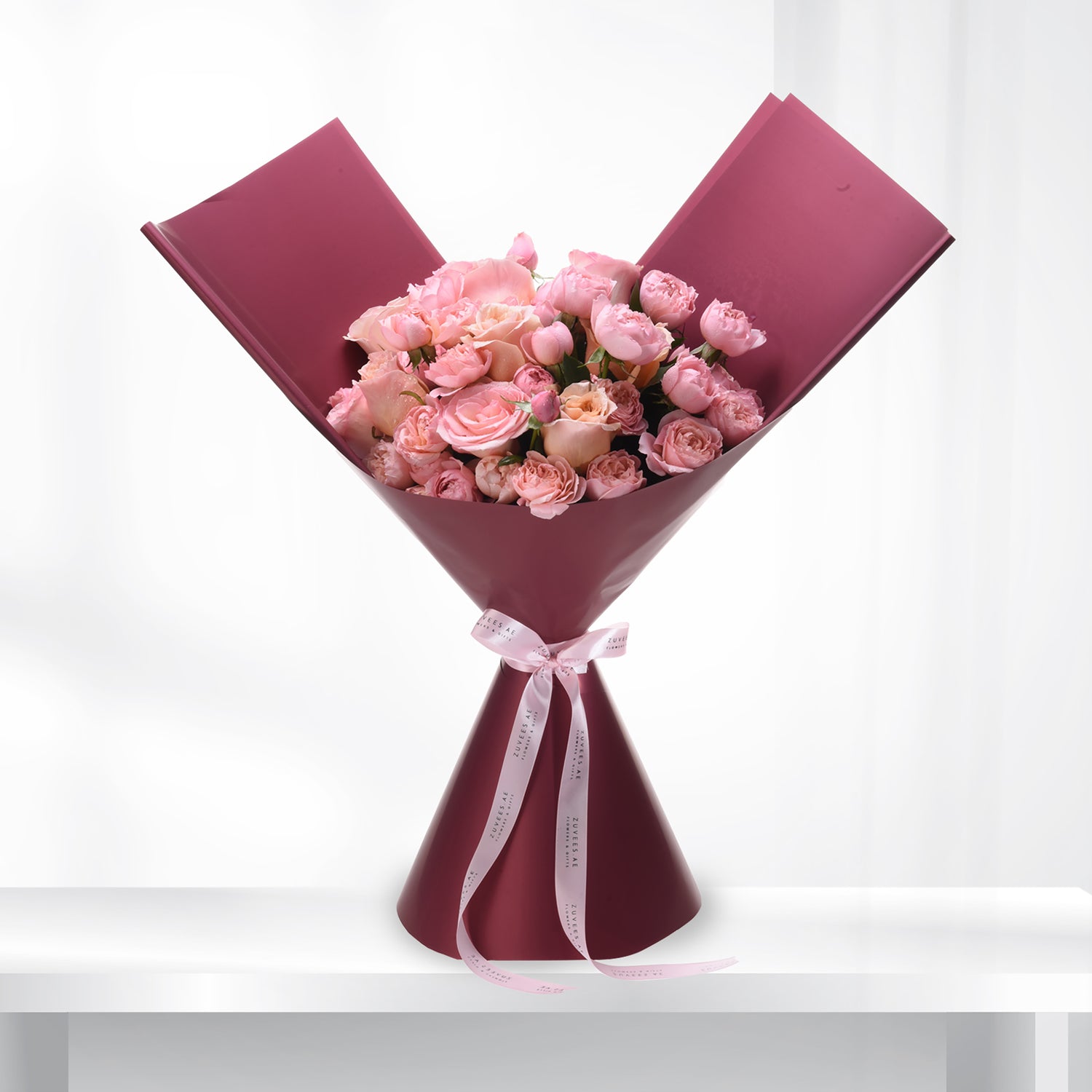 Soft pink roses in burgundy wrap, elegant ribbon bow, minimalist white background.