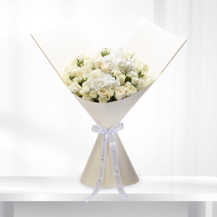 Elegant white rose and hydrangea bouquet wrapped in cream paper with branded ribbon.