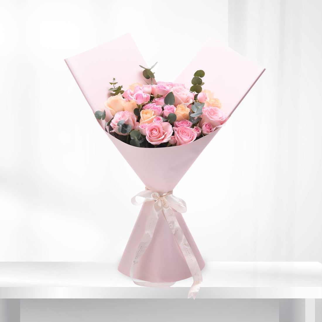 Soft pink roses and eucalyptus wrapped in pastel paper with elegant ribbon.