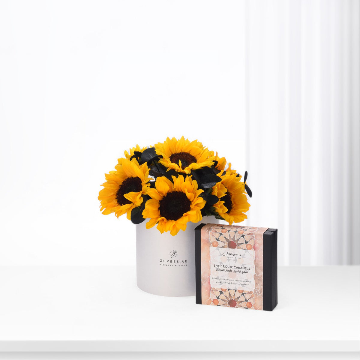 Vibrant sunflowers in white vase beside ornate caramel gift box.