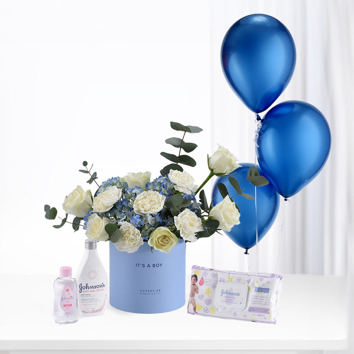Blue balloon bouquet with white roses, Johnson’s baby essentials, and “It’s a Boy” gift box.