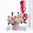 Pink floral arrangement with balloons, baby essentials, and "It&