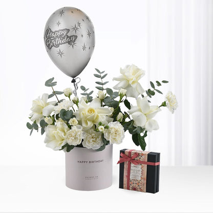 Silver balloon, white roses, eucalyptus, and chocolate gift box in minimalist birthday arrangement.
