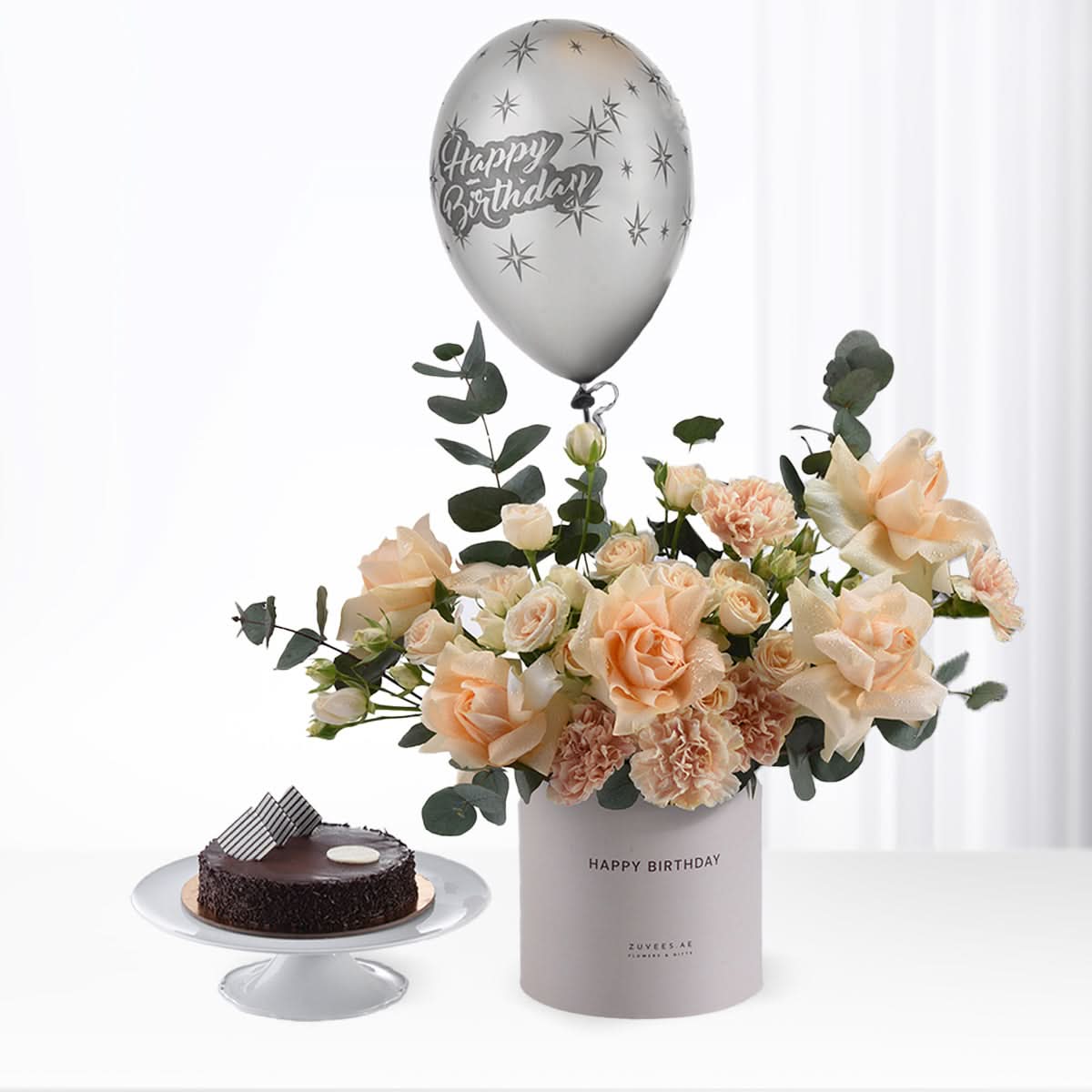 Silver balloon, peach roses, chocolate cake—birthday celebration centerpiece.