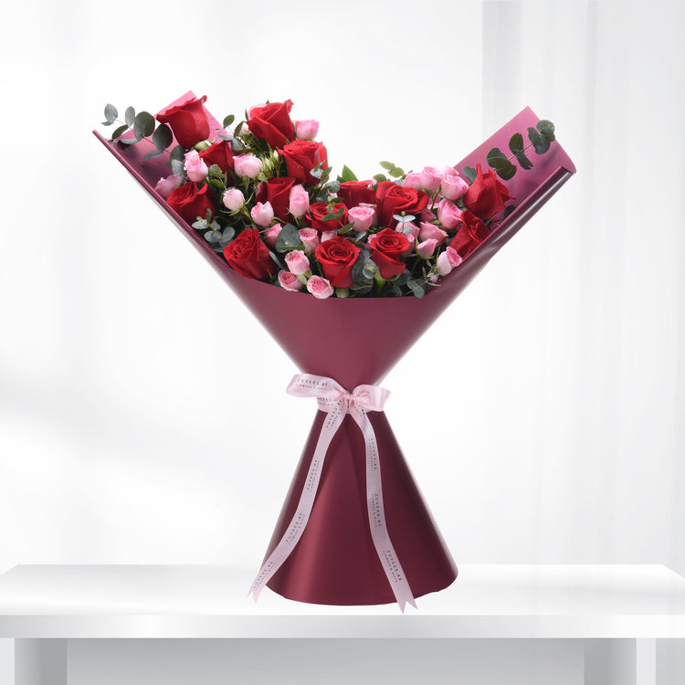 Vibrant red and pink roses in burgundy wrap, accented with eucalyptus and branded ribbon.