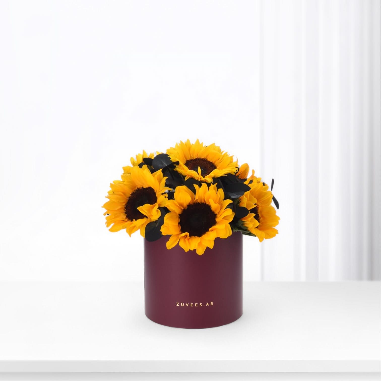 Vibrant sunflowers in burgundy cylinder vase with gold branding.