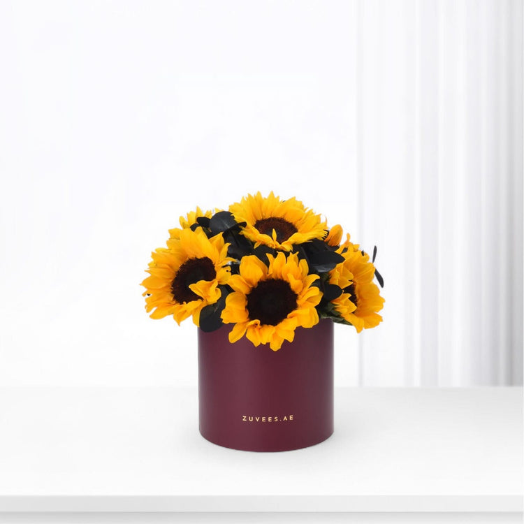 Vibrant sunflowers in burgundy cylinder vase with gold branding.