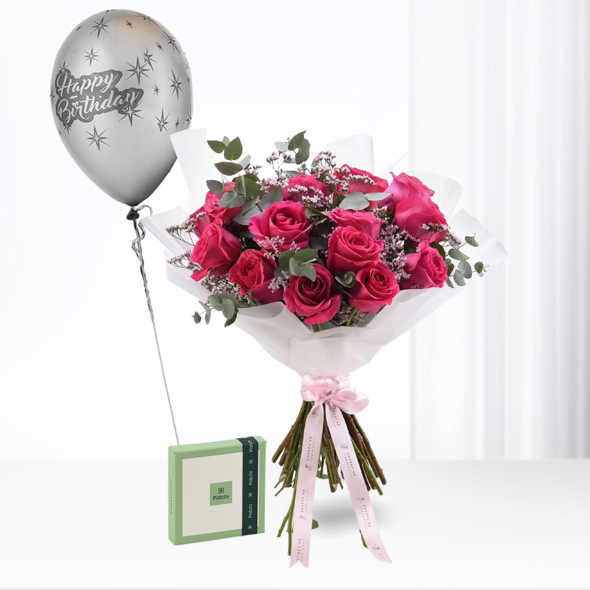 Vibrant pink roses, silver birthday balloon, and green gift box elegantly arranged.