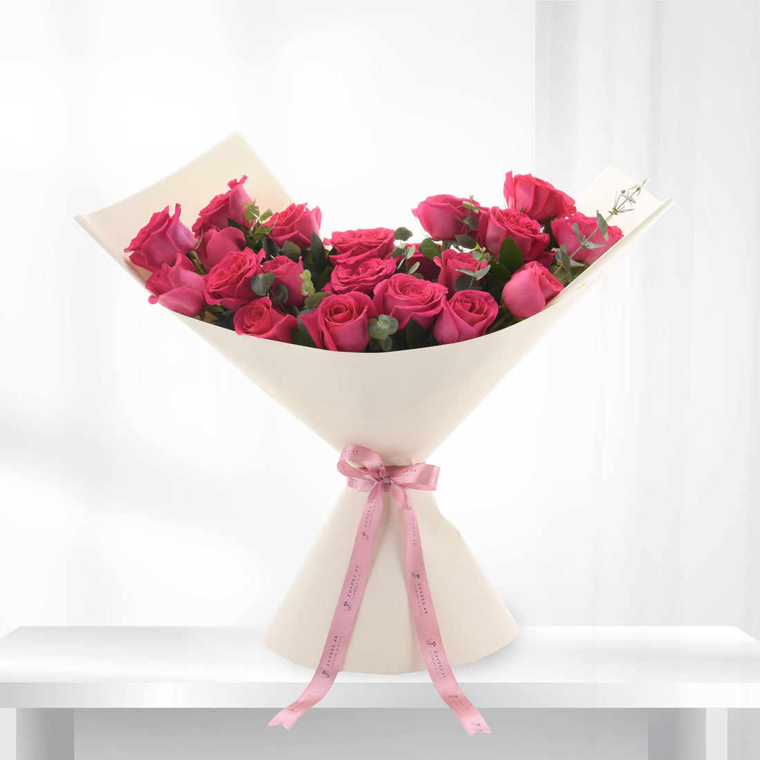 Vibrant pink roses in cream wrap, accented with pink ribbon.