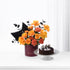 Vibrant orange roses, coral carnations, black foliage in burgundy Zuvees vase beside chocolate cake.