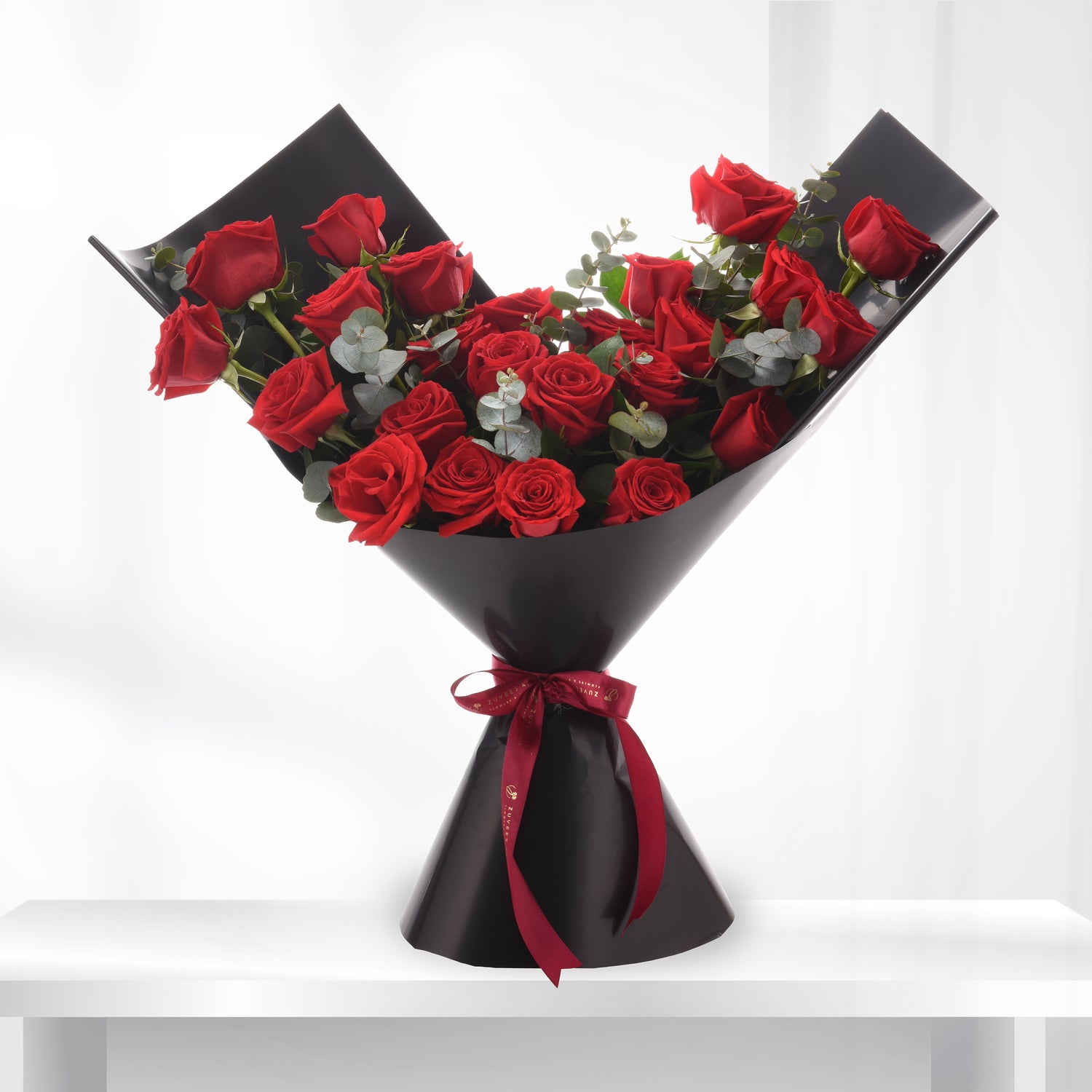 Vibrant red roses in sleek black wrap, accented with eucalyptus and a crimson bow.