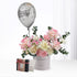 Silver balloon floats above pastel pink/white roses and eucalyptus in a “Happy Birthday” vase, beside a gift box.