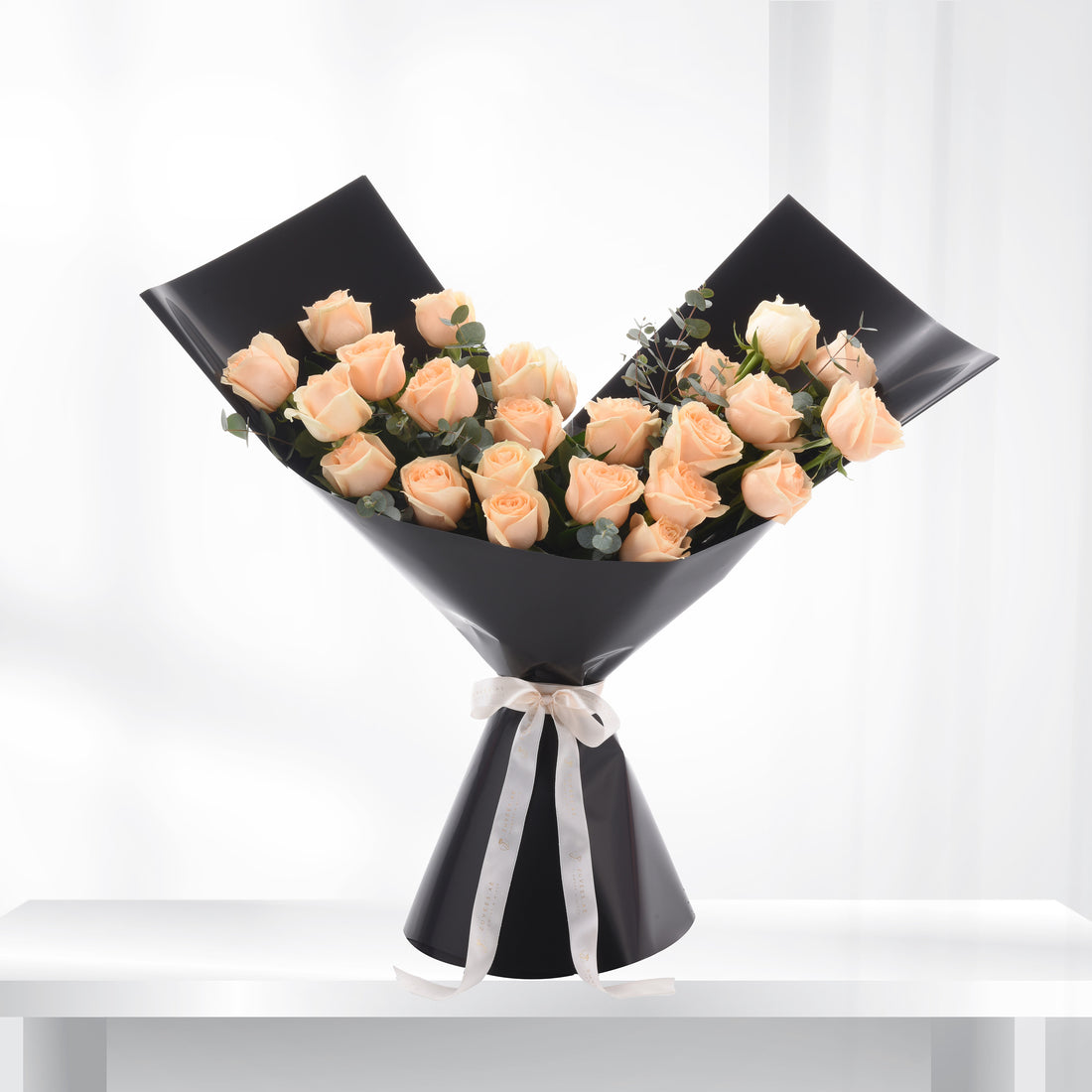 Elegant peach roses in sleek black wrap, accented with eucalyptus and ivory ribbon.