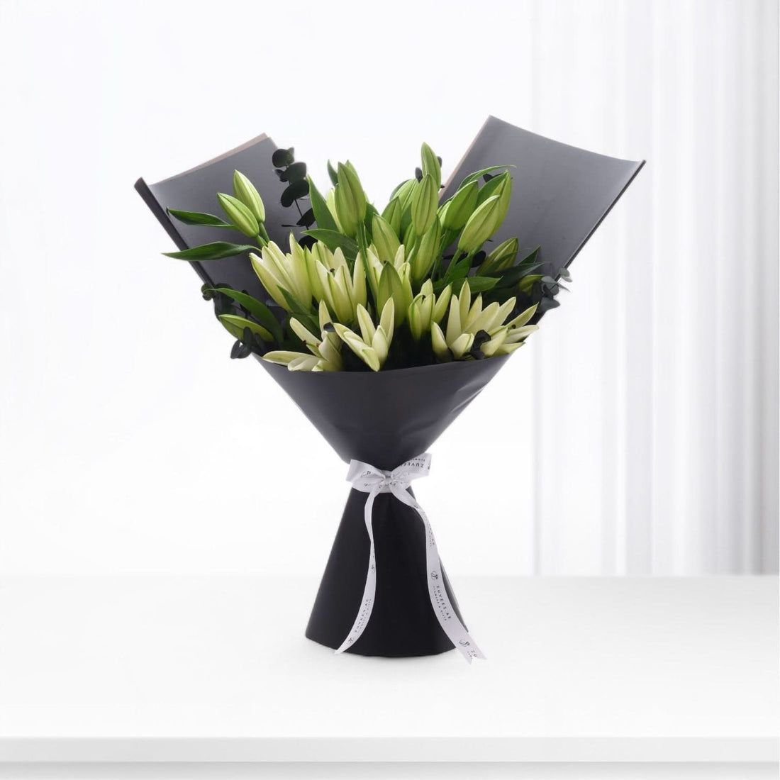 Elegant black-wrapped bouquet of creamy white lilies with green buds and eucalyptus.
