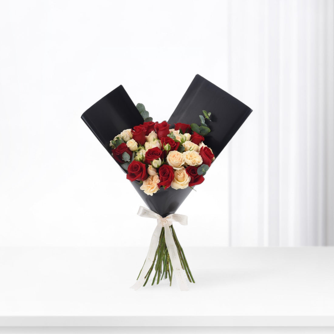 Elegant black-wrapped bouquet with red and cream roses, accented by eucalyptus and a white ribbon.
