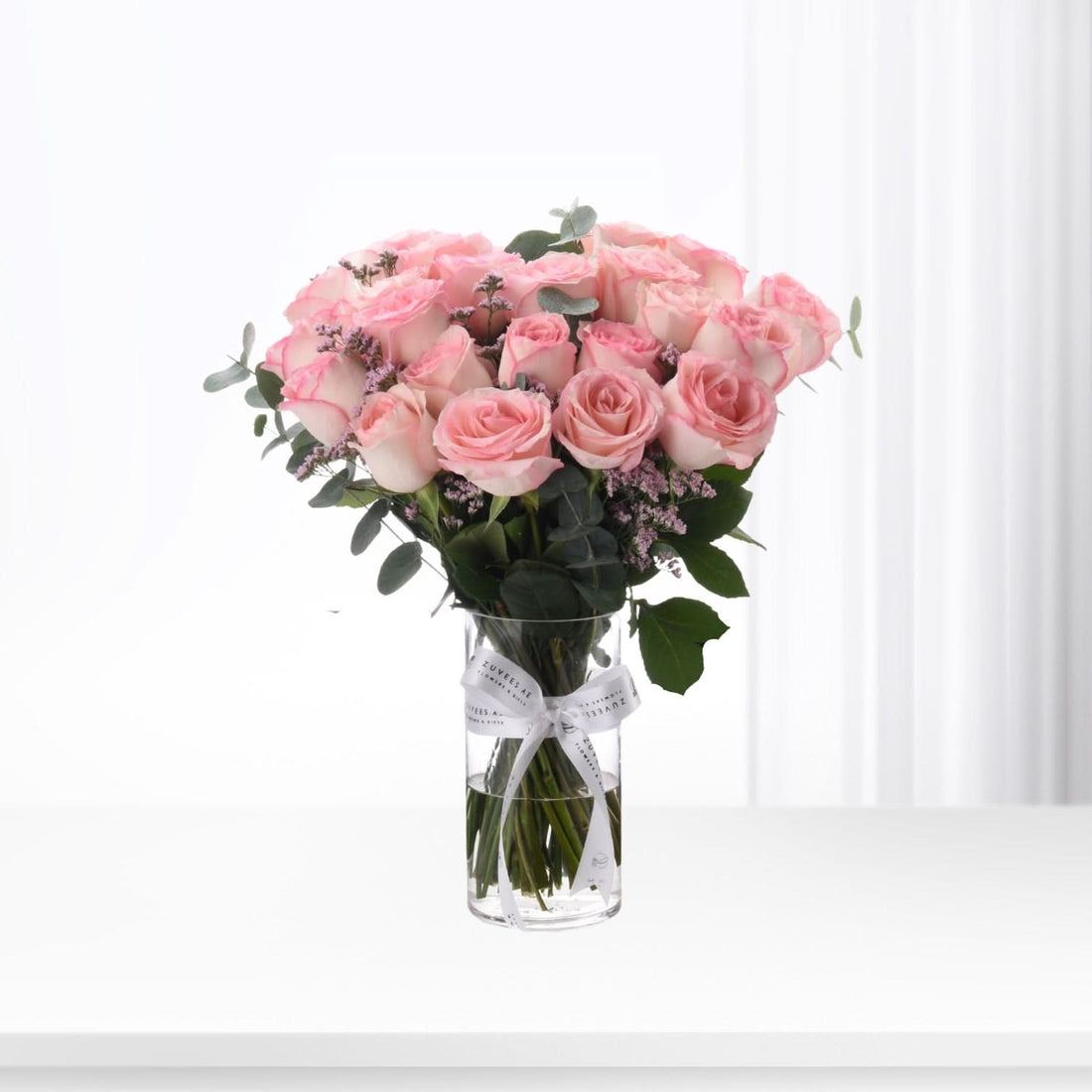 Soft pink roses in clear vase, accented with greenery and lavender, tied with white ribbon.