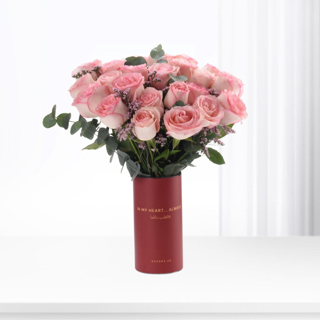 Soft pink roses in red tube vase with gold text, elegant floral gift.