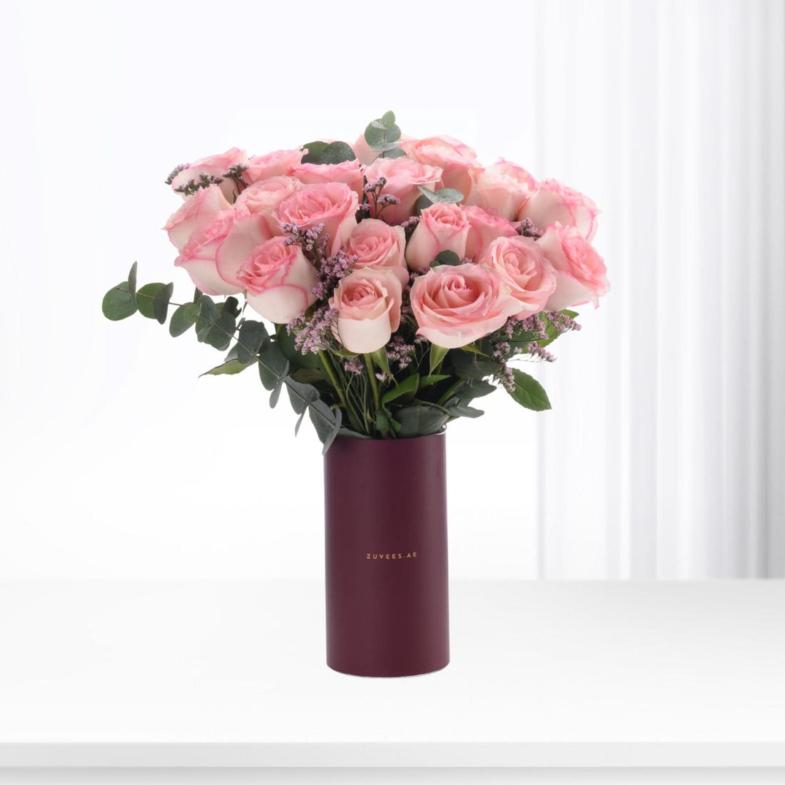 Soft pink roses in deep burgundy vase with eucalyptus and lavender accents.