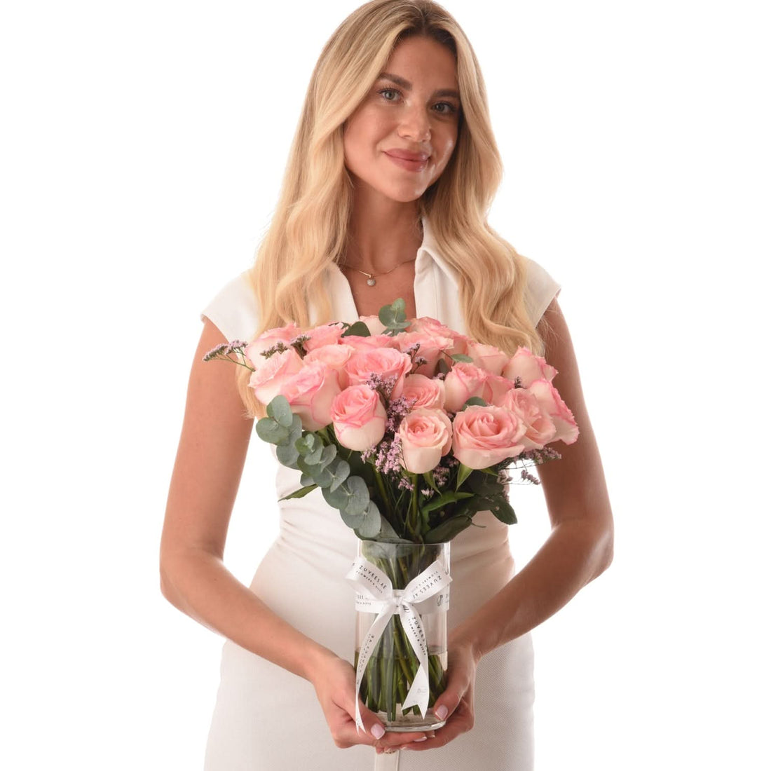 Woman holds lush pink rose bouquet in clear glass vase with white ribbon.
