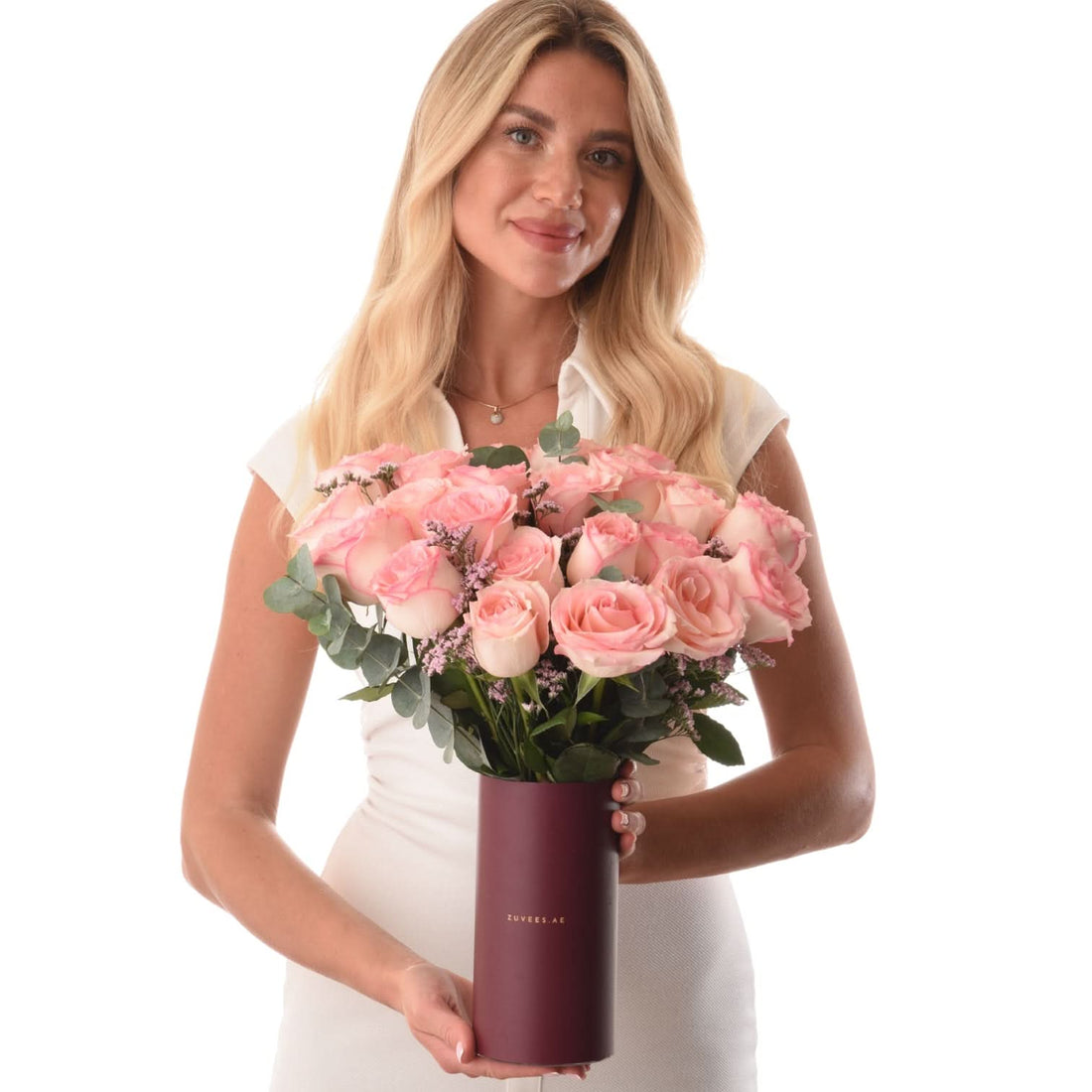 Woman holds lush pink rose bouquet in matte burgundy tube vase.