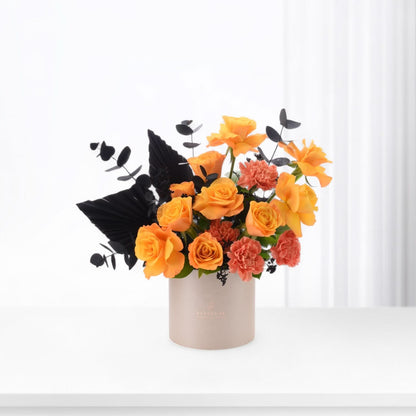 Vibrant orange roses and coral carnations contrasted with dramatic black foliage in minimalist beige vase.