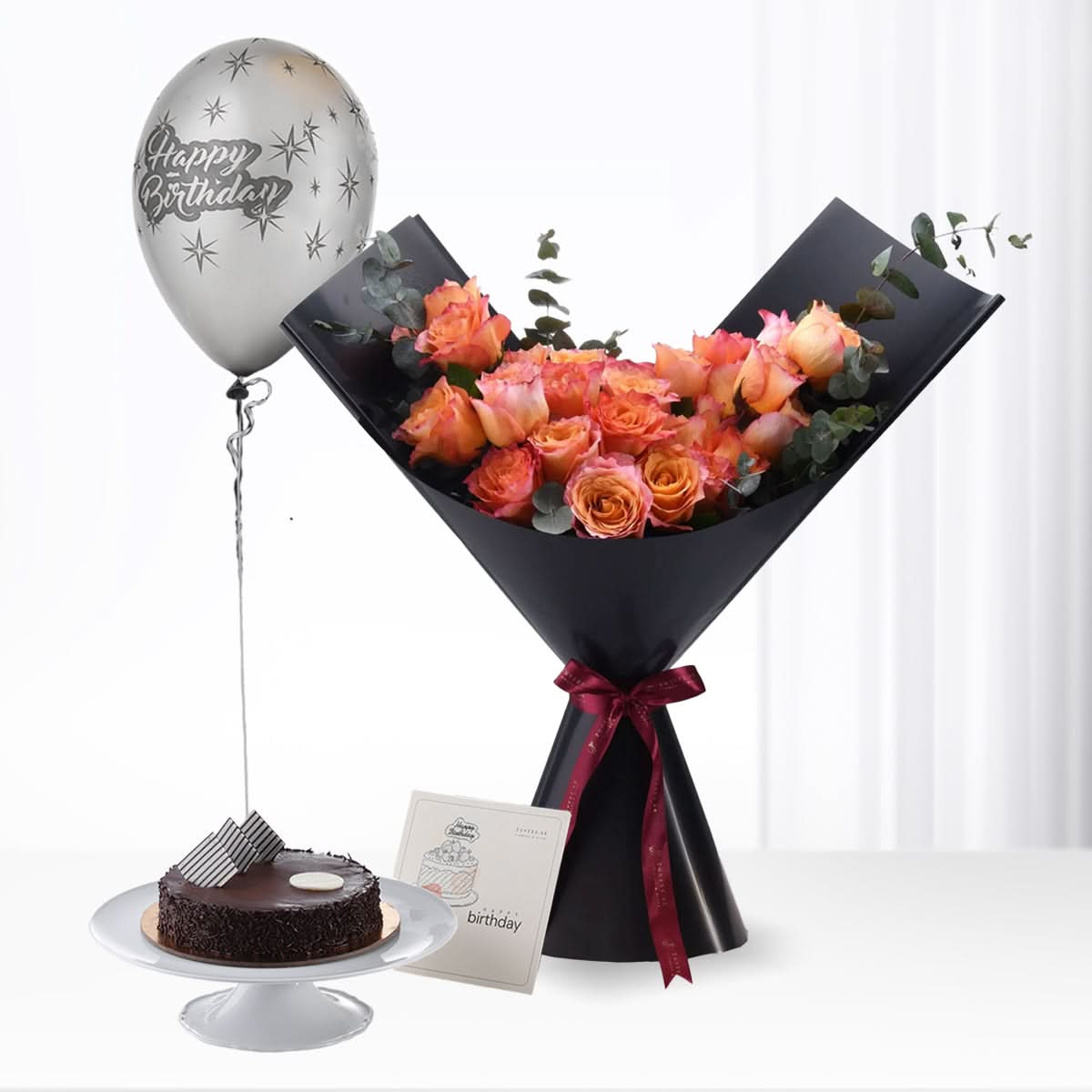 Orange roses in black wrap, chocolate cake, silver birthday balloon.
