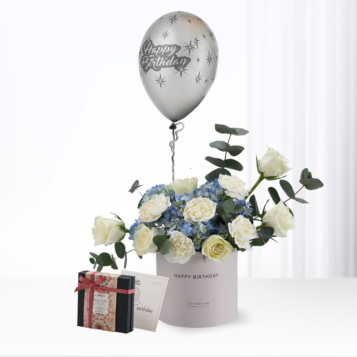 Silver balloon floats above white roses and blue hydrangeas in a birthday-themed vase.