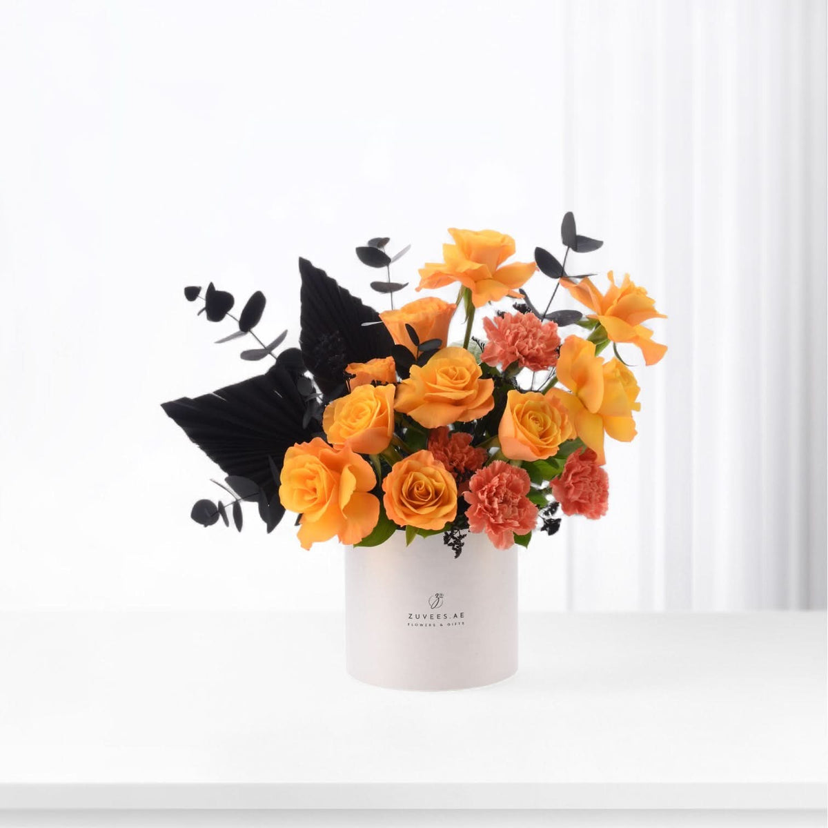 Vibrant orange roses, coral carnations, black foliage in sleek white Zuvees vase, minimalist modern aesthetic.